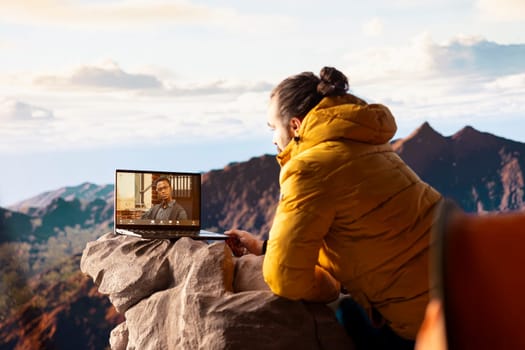 Young CEO entering a video call from the mountain top with a strong signal, always connected and discussing with associates about business matters. Workaholic businessman hiking.