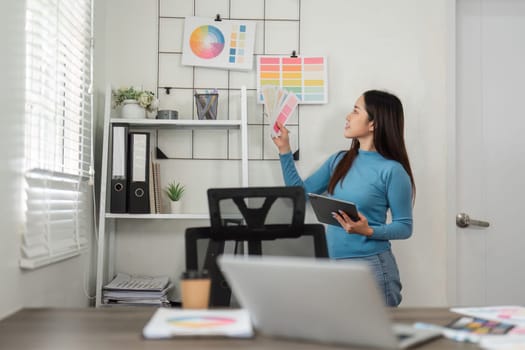 In the midst of a design process, a woman evaluates color swatches, contemplating the combination of hues for her project in a bright workspace.