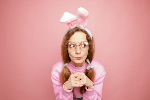 Playful woman in pink sweater and bunny ears making a funny expression. Quirky Easter concept, humorous portrait, festive mood, and spring vibes