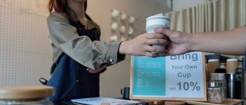 A barista provides a customer with a reusable cup, highlighting a discount incentive for choosing sustainable practices in a cafe.