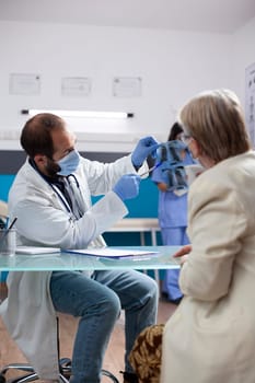 Male doctor discusses lung xray with female pensioner patient during elderly consultation in hospital. Bearded doctor and old woman examining radiograph diagnosis during medical checkup.
