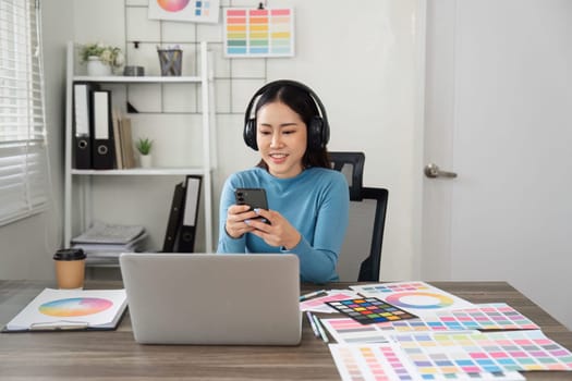 A designer combines casual communication with focused creativity, holding a phone while analyzing colorful design swatches in their workspace.