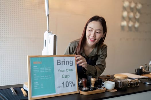 A barista prepares a sign promoting a discount for customers who bring their own cups, supporting sustainable practices in the cafe.