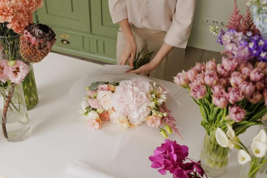 Female florist creating a delicate bouquet with fresh flowers in a floral workshop, surrounded by colorful blooms in glass vases. flower shop