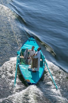 Esna, Egypt - 3 November 2024: Street vendor in a small rowboat selling textiles while attached and being towed by a cruise ship.
