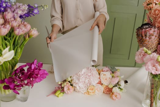Florist wrapping a fresh bouquet in elegant paper, preparing a stylish floral arrangement for gifting or sale. flower shop