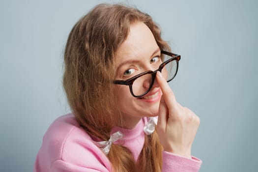A woman with long hair and glasses playfully adjusts her glasses, smiling at the camera. She is wearing a pink sweater, concept vision problem