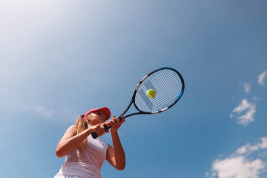Young female tennis player preparing to hit a ball with a racket against a bright blue sky background., tennis game