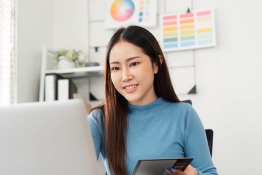 A smiling young woman is working on her laptop with color palettes, showcasing the joy of creativity in a professional setting.