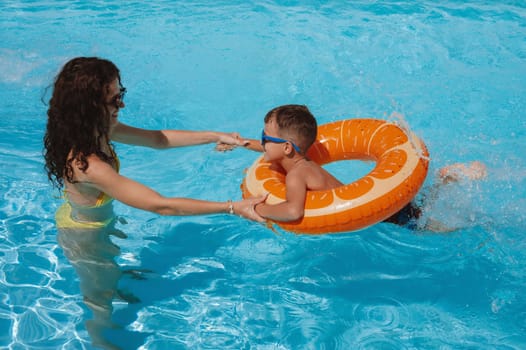 young mother teaches her child boy son to swim in swimming pool at a hotel on vacation at a resort in the summer