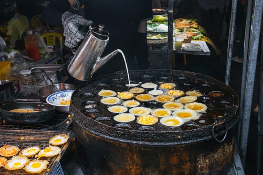 cooking a traditional Vietnamese dish Banh Khot with shrimps and corn at an Asian night market on street in Vietnam in Asia