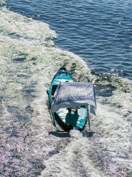 Street vendor in a small rowboat selling textiles while attached and being towed by a cruise ship.