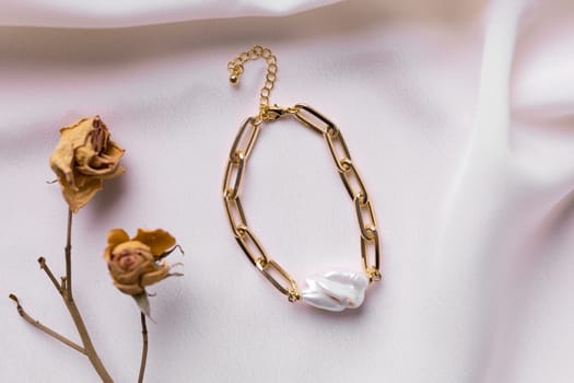 Jewelry on satin fabric with gold pearl bracelets and dry flowers elements. Handmade bijouterie and natural aesthetics in fashion.