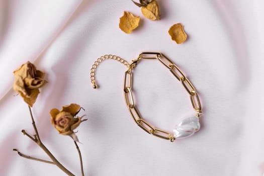Jewelry on satin fabric with gold pearl bracelets and dry flowers elements. Handmade bijouterie and natural aesthetics in fashion.