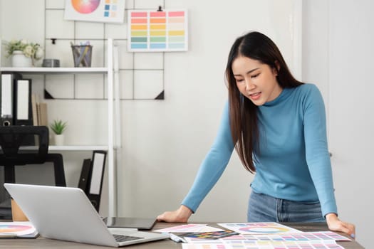 A female designer examines color samples and design materials on her desk, deeply focused on her creative project in a contemporary office environment.