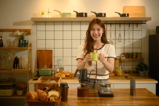 Happy asian woman wearing an apron preparing coffee with a manual grinder and pour over setup.