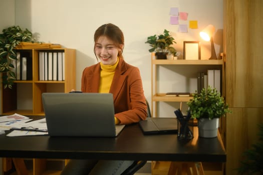Smiling young businesswoman working on a laptop in a cozy, modern home office.