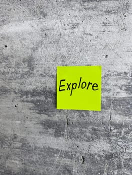 Bright yellow sticky note with the word Explore prominently displayed on a textured grey background, signifying the spirit of adventure and the pursuit of new experiences