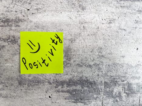 Sticky note displaying the word Positivity along with smiley face on a textured grey surface, embodying the spirit of optimism and the importance of a positive attitude in everyday life