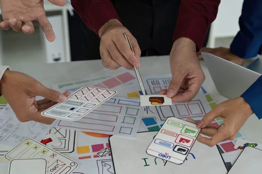 Collaborators analyze design elements and share creative insights while holding paper prototypes, fostering a productive design environment.