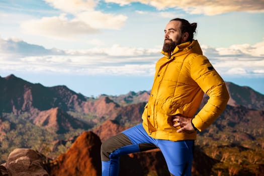 Male hiker looks out over a breathtaking mountain range from the hill top, embracing the solitude and fresh air of the great outdoors. Sense of adventure and endless nature exploration.
