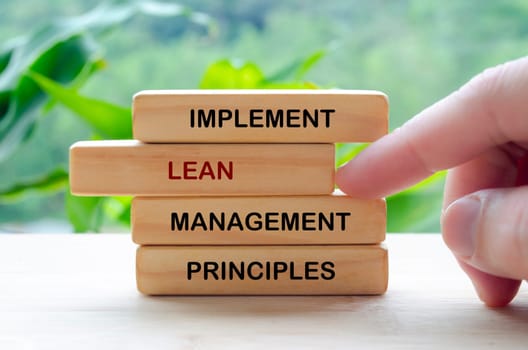 Implement Lean Management Principles text on wooden blocks representing continuous improvement strategy.