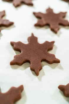 Overhead view of raw Chocolate Ginger Sugar Cookies in snowflake shapes arranged neatly on a parchment-lined baking tray, ready to bake.