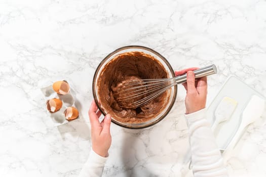 Flat lay. With a hand whisk, the ingredients are expertly mixed in a glass mixing bowl - creating this delectable Chocolate Bundt Cake.