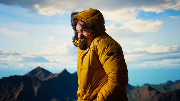 Young traveler struggling with cold winds on top of the mountain, feeling proud of his trekking activity. Adventure seeker with ambition successfully climbing the mountain range. Camera A.