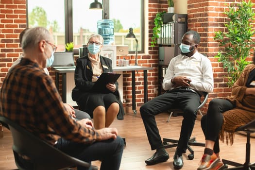 Retired female therapist leading group counselling session, having moments of honest conversation among participants. Elderly woman with clipboard giving mental health advice to patients at therapy.
