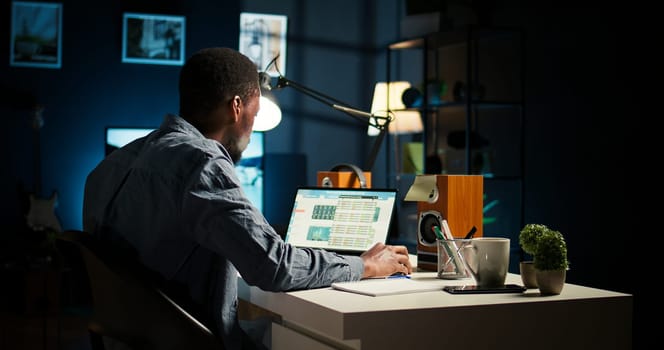 African American teleworker managing daily schedule and does post it memo notes, creating a reminder to ensure task completion from his home office. Freelancer improving productivity. Camera A.