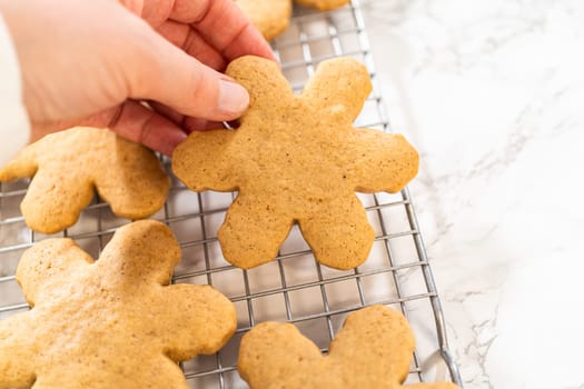 Close-up side view of a hand holding a freshly baked snowflake-shaped amber gingerbread cookie over a cooling rack, showcasing its intricate festive design and golden-brown texture.