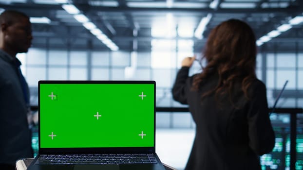 Mockup laptop in front of software developers walking in data center, reviewing equipment diagnostics. Close up of isolated screen notebook next to teamworking IT professionals in server farm