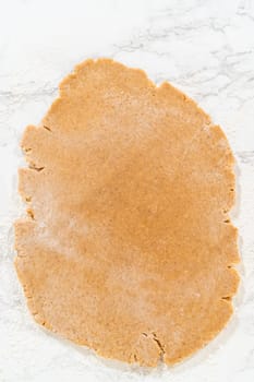 Overhead view of amber gingerbread cookie dough rolled into a large, thin, evenly flattened layer on a lightly floured marble surface, ready for shaping.