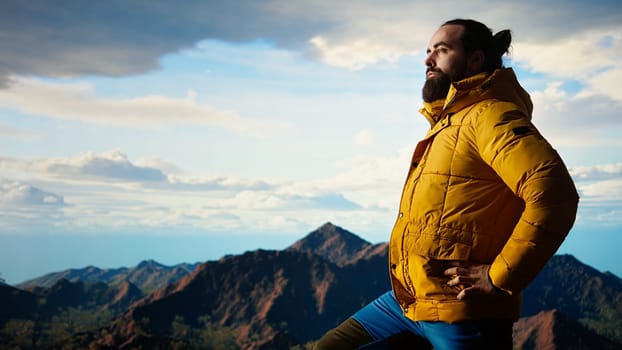 Nature lover stands at the edge of a breathtaking mountain range, looking at the scenic background of towering peaks and vast sky. Young man enjoying adventure and outdoor exploration. Camera A.