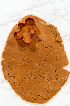 Close-up of a cookie cutter pressing into gingerbread dough on a floured surface.