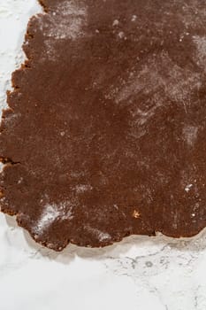 Overhead view of chocolate cookie dough partially rolled out on a floured marble surface, prepped for cookie cutting.