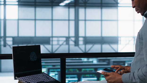 Technician in data center with laptop and tablet integrating AI driven automation tools. Server room worker using artificial intelligence on devices, ensuring continuous uptime, camera A