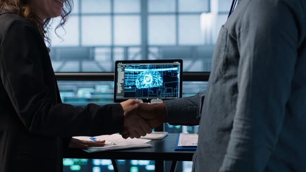 Manager meeting with client in data center using artificial intelligence tech, reaching deal. People doing handshake in AI based server farm after checking files and finishing transaction, camera A