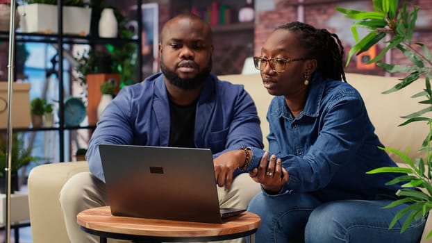 African american couple work on a management project for freelancing, using a laptop to research business trends and manage an online brand. Successful remote career development. Camera B.
