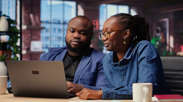 Black freelancers team at home desk using laptop and checking emails, reading messages in inbox and solving their daily tasks. Couple managing electronic correspondence. Camera B.