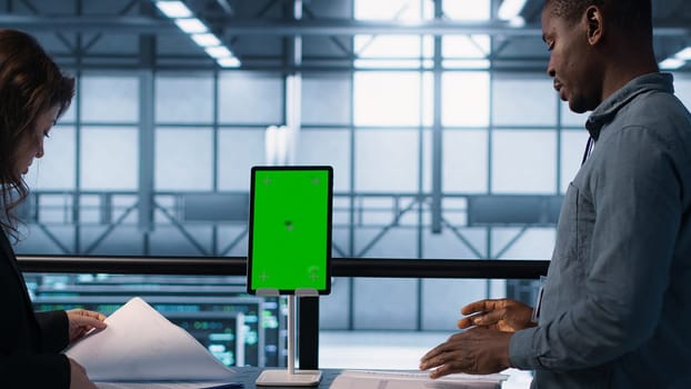 Inspector checking documents in server hub to ensure compliance with industry standards, using mockup tablet. Admin team inspecting files, overseeing data center workplace security protocols, camera A