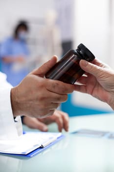 Closeup of hands of caucasian people holding container of prescribed medicine at desk in medical office. Physician handing over health supplements to patient during clinic appointment.