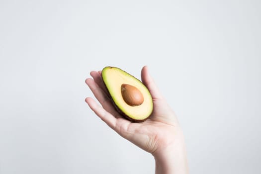 Hand holding half avocado against white background.