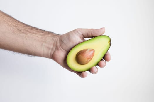 Male hand holding fresh half avocado against white background.