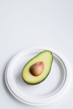 Halved ripe avocado on white plate against minimalistic background.
