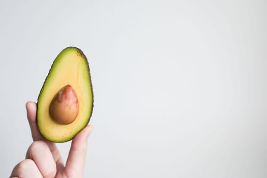 Hand holding halved avocado against minimalist white background.