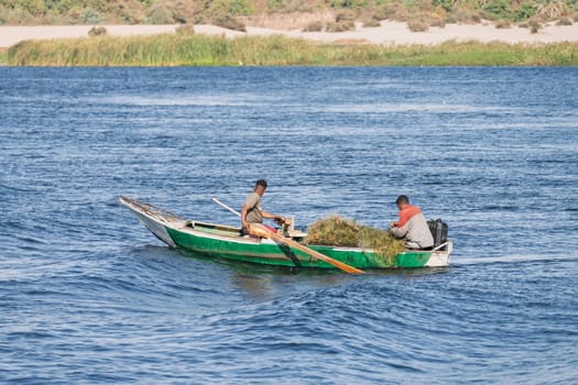 Fishermen in rowing boat caught in waves from a passing cruise boat after collecting fishing net from Nile