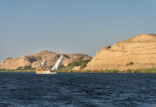 Edfu, Egypt - 3 November 2024: Small river cruise boat Amunet sails down the Nile with Sahara desert behind