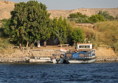 Edfu, Egypt - 3 November 2024: Small passenger ferry boat by the banks of the Nile with the Sahara desert behind